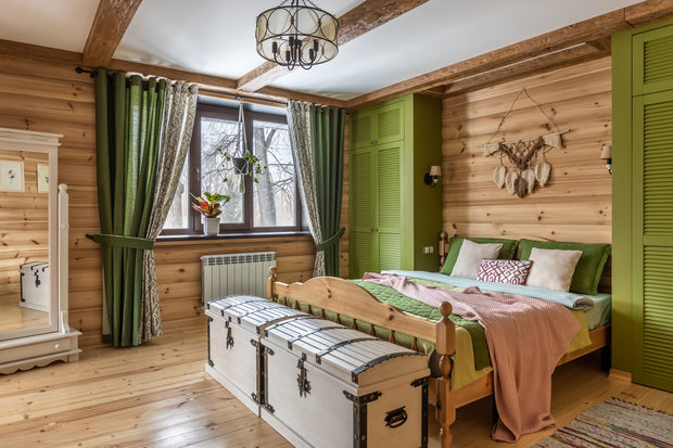 В спальне хотелось немного поиграть, поэкспериментировать: так в изголовье появились шкафы травянисто-зеленого цвета. Резная кровать и зеркало, сундуки и комод с ковкой, коврики в полоску напоминают о деревенском доме.