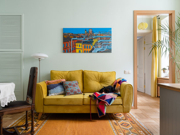 А вот диван современный. К нему подобрали яркую картину с видами Петербурга. Желтый цвет обивки поддержали желтыми шторами, которые добавляют ярких красок в пасмурные дни.