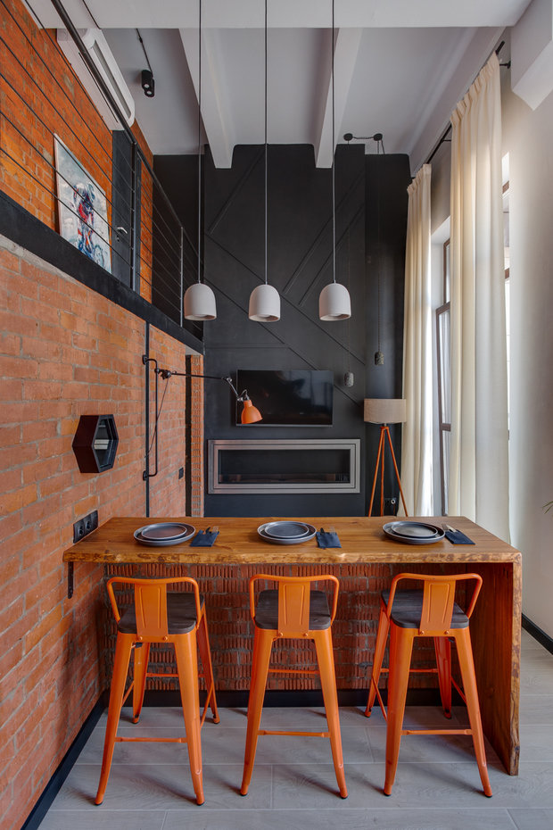 Барный стол выполнен на заказ из натурального дерева. Его расположили так, чтобы удобно было смотреть телевизор или на камин, а также работать за ноутбуком, если будет такая необходимость. Барные стулья выбрали в оранжевом цвете.