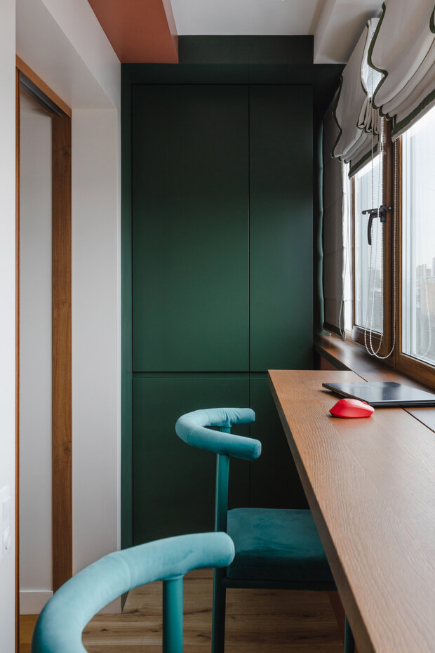 Боковые стены лоджии выкрасили в насыщенный темно-зеленый цвет. С одной стороны интегрировали встроенный шкаф для хранения с фасадами в цвет стены, а с другой организовали мини-рабочий кабинет.