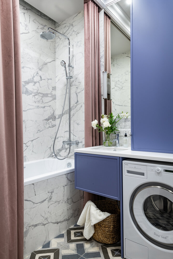 Текстильная портьера со стороны раковины добавляет уюта помещению. Со стороны ванны — обычная белая шторка, которая закрывается, когда необходимо принять душ. Также привлекает внимание ярко-фиолетовый акцентный шкаф, где разместили и зону умывания, и зону стирки, и зону хранения.