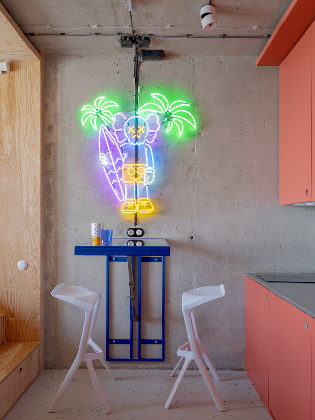 На бетонной стене разместили неоновую вывеску с яркими цветами, она создает уютную атмосферу в вечернее время и навевает мысли о тропических странах, океане и серфинге.