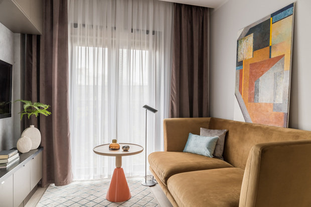 На светлом фоне ярким акцентом выделяется стильный диван и дизайнерский журнальный столик. ТВ вписали между напольной и подвесной системой хранения.