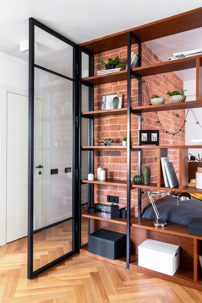 Для согласования двери в санузел, выходящей в жилую комнату, спроектировали стеклянную перегородку с возможностью ее расположения в двух положениях. В открытом формате она служит для зонирования коридора, при этом она может складываться и превращаться в стеклянную дверцу стеллажа, не перегружающую единое пространство гостиной.