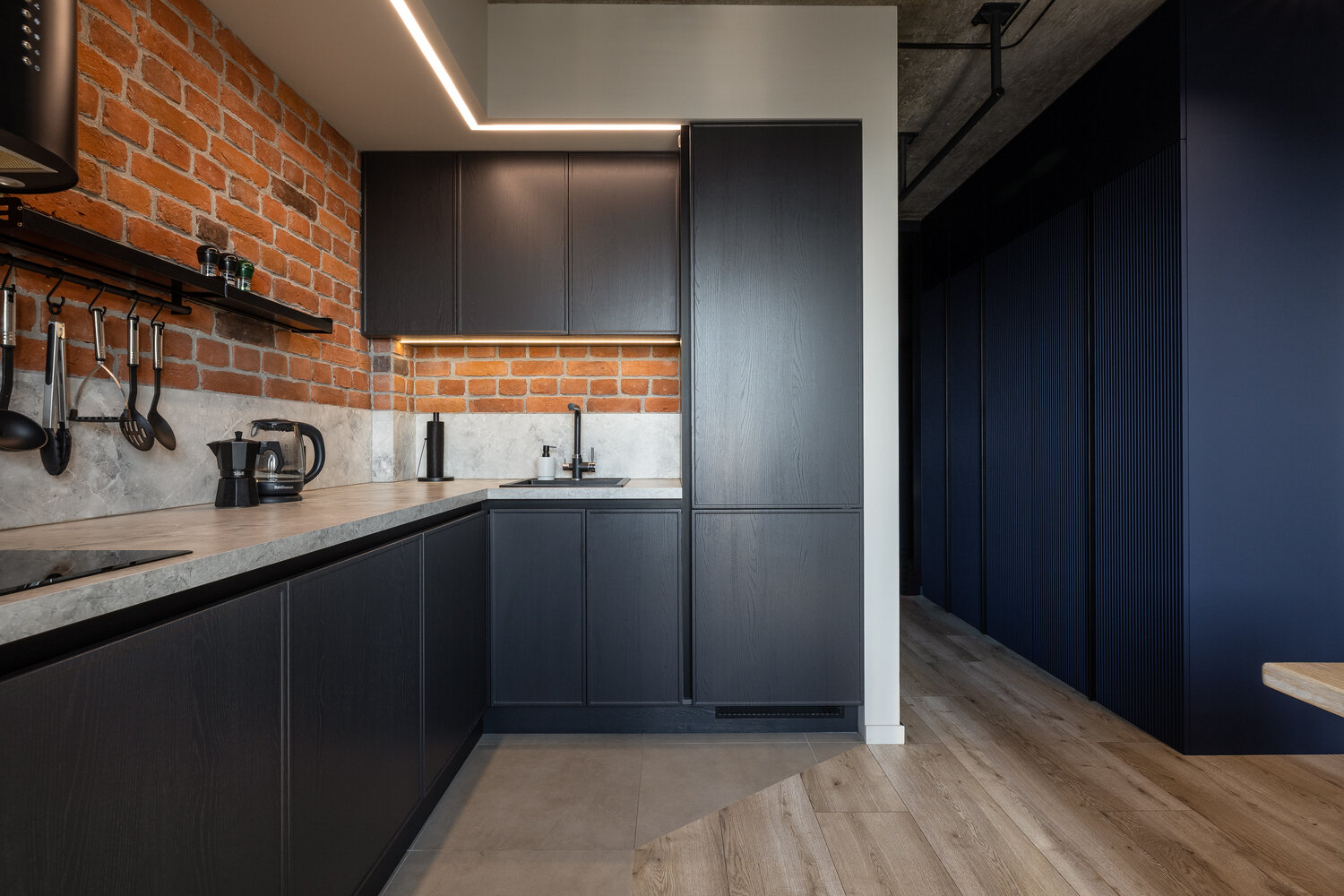 Фасады графитового оттенка дополнили столешницей и мини-фартуком из искусственного камня. Они отлично сочетаются с фактурой кирпича.