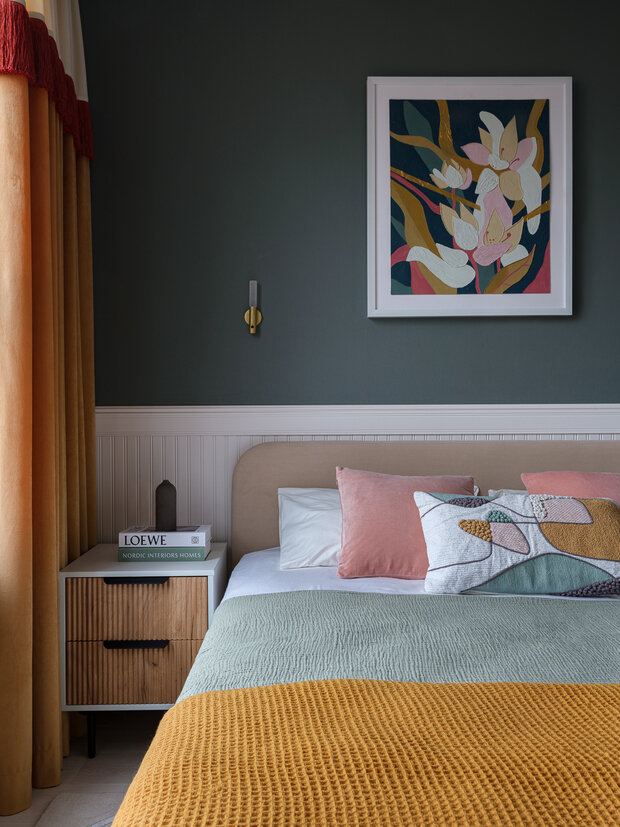 Для декоративного текстильного оформления кровати были подобраны две розовые подушки к розовому стулу и одна декоративная подушка с рисунком. К ним взяли муслиновое покрывало мятного цвета и в качестве акцента — шерстяной теплый плед горчичного оттенка. Над изголовьем — искусство в белой раме от галереи Art Melete. Абстрактная цветочная композиция была написана как будто специально для этого интерьера — в ней присутствовали все оттенки комнаты, она отлично вписалась в стилистику.