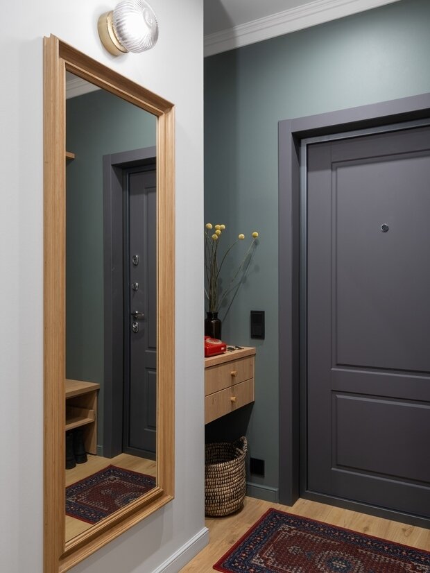 В прихожей сразу при входе расположен канализационный стояк, горячая и холодная вода. В процессе ремонта не стали зашивать всю зону наглухо и оставили нишу, в которой разместили небольшую консоль с ящиком для мелочей. Доступ к коммуникациям организован сбоку (предусмотрен люк под покраску).