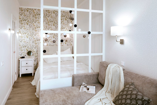 Зонирование в жилой комнате сделали при помощи перегородки из МДФ. Таким образом ограничили приватную зону — спальню. В изголовье кровати поклеили скандинавские обои с цветочным орнаментом — получилось очень уютно.