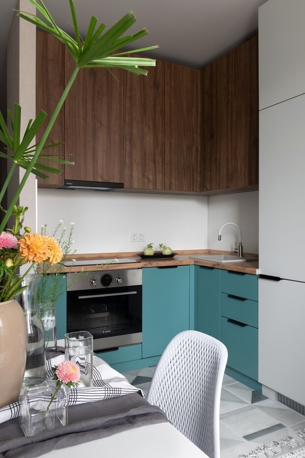 Для поддержки акцентного цвета морской волны дизайнеры добавили его в фасады в сочетании с текстурой дерева. Так получилась небольшая, но яркая мебельная композиция, собирающая образ кухни-столовой-гостиной.