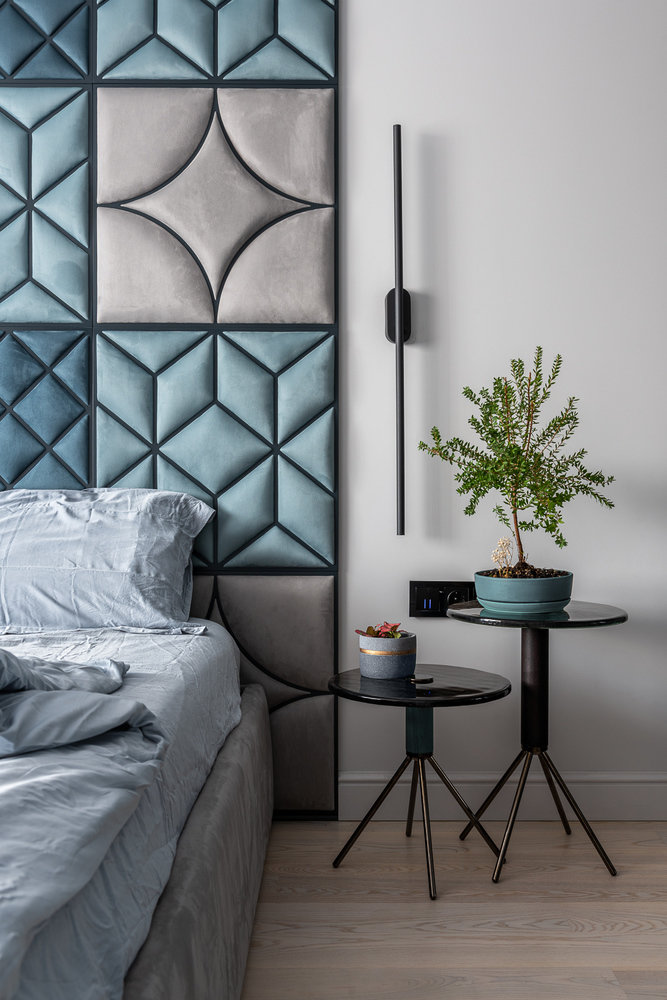 В качестве прикроватных тумбочек решили остановиться на столиках. Ножки поддержали бра на стене, а стеклянная столешница подружилась с фасадами шкафа. Органический декор в виде цветов в горшках добавил нужной атмосферы.