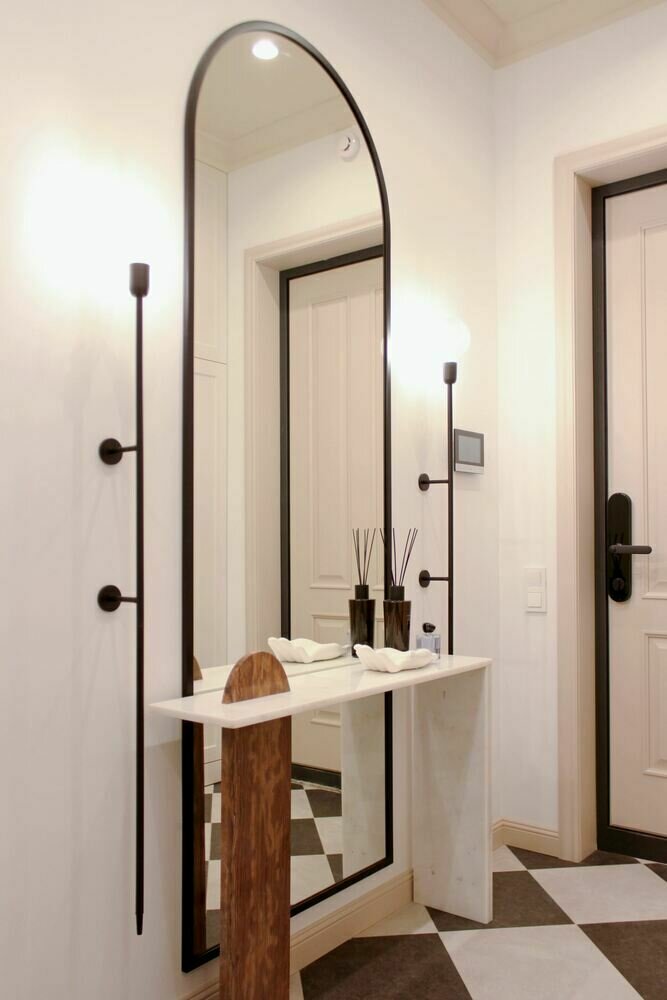 Самый яркий и запоминающийся предмет интерьера — это асимметричная мраморная консоль в прихожей. Два разных вида мрамора разных геометрических форм перекликаются, создавая один необычный предмет интерьера. Кстати, арочная мраморная деталь повторяет форму зеркала, а также арок в коридоре.