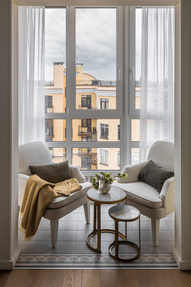 Балкон утеплили, положили плитку. Для зоны отдыха выбрали пару одинаковых кресел со светлой обивкой и комплект кофейных столиков со столешницей из камня. 