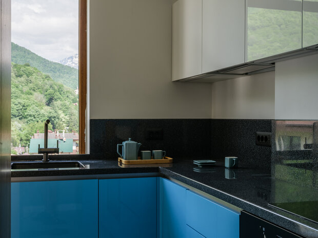 Раковину расположили с видом на горы. Кран выбрали в темном никеле. Фартук из акрилового камня подняли над столешницей на 30 см.