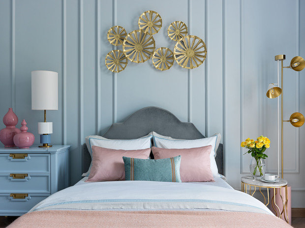 Пространство комнаты решили обыграть асимметрично, не по законам классики. Поэтому с одной стороны кровати стоит вместительный комод, а с другой — легкий латунный столик с торшером.