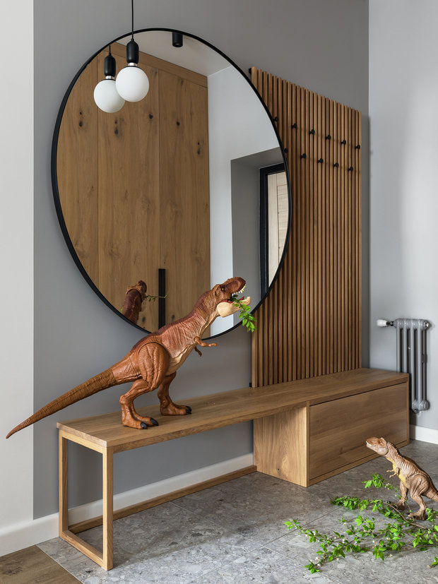 В зоне прихожей предусмотрели большой шкаф для хранения верхней одежды и хозяйственных принадлежностей (на фото он отражается в зеркале).  Напротив создали функциональную архитектурную композицию из большого круглого зеркала, настенной вешалки и скамьи.