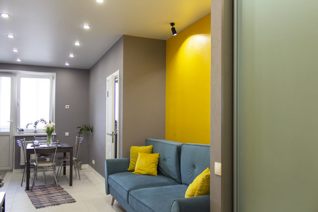 Интерьер гостиной в современном стиле с синим диваном и желтой стеной