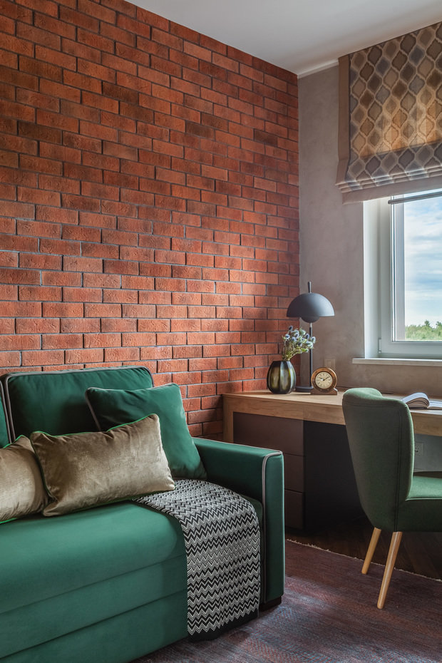 Одну из стен в кабинете оформили красным кирпичом. На его фоне особенно эффектно смотрится зеленый диван. 