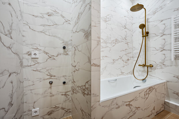 Интерьер ванной комнаты в современном стиле с отделкой под мрамор и золотыми смесителями