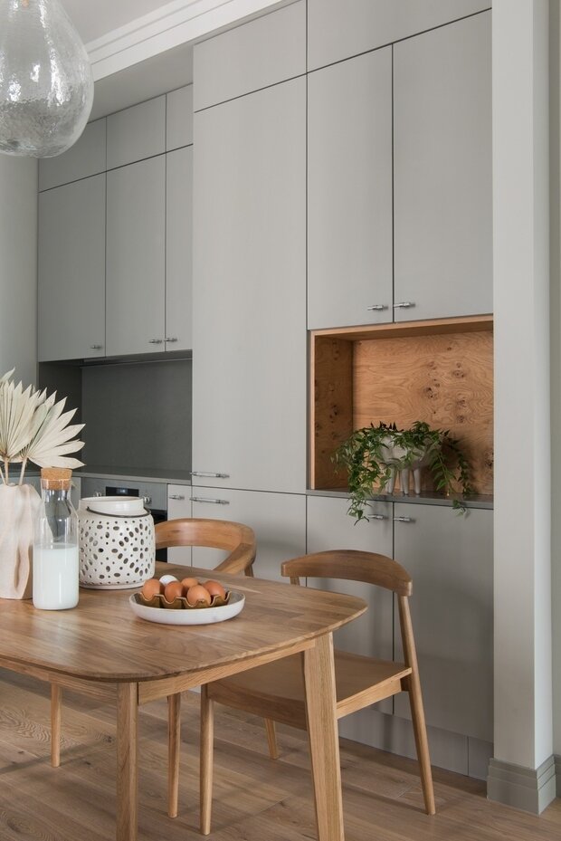 Встроенный шкаф с деревянной нишей на кухне имеет меньшую глубину, хотя и выведен в одну линию с кухней — это позволило выделить место для колонны со стиральной техникой в примыкающем санузле.