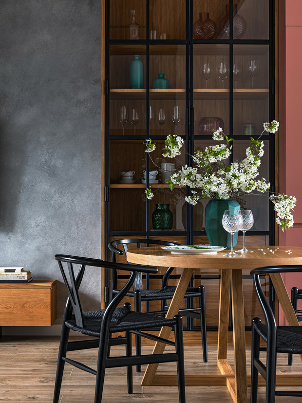 Зоной, объединяющей кухню и гостиную, служит обеденная группа с круглым раскладным столом, выполненным по чертежам дизайнеров из массива дуба. Высокий шкаф-витрина со стеклянными фасадами отлично сочетается с дверями в кабинет.