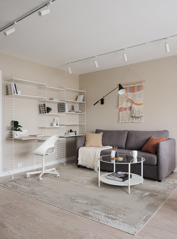 В гостиной система стеллажей в духе скандинавского дизайна, выполненная на заказ. В систему интегрировано небольшое рабочее место. Стеллаж вмещает книги и декор.