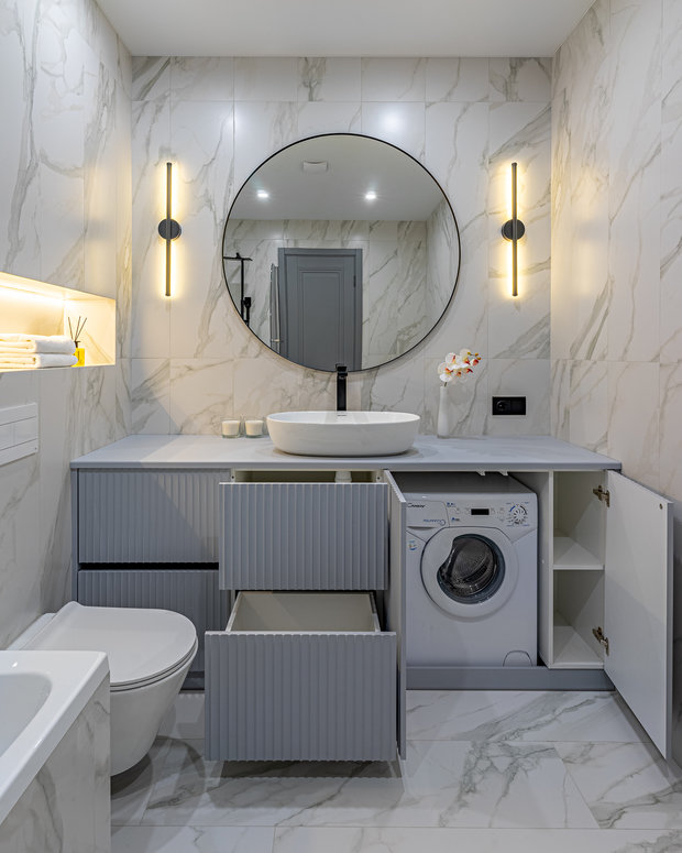 Изящная тумба была выполнена под заказ, в нее встроена стиральная машина. Установлены подсветка ниши и теплое освещение у зеркала. 