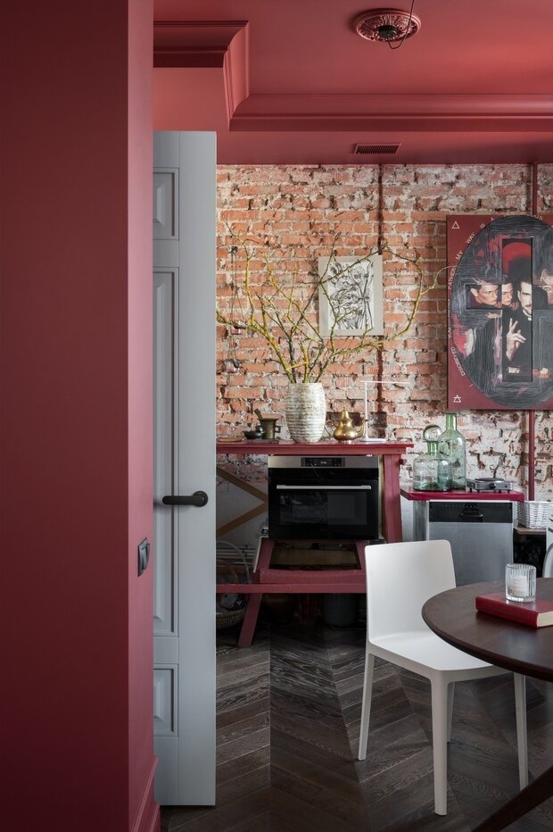 На момент фотосъемки квартиры вместо кухонного гарнитура использовались строительные леса, которые остались от строительной бригады после ремонта. Дизайнер эти леса покрасила в цвет стен (благородный бордовый оттенок) и разместила в них духовой шкаф и посудомоечную машину.