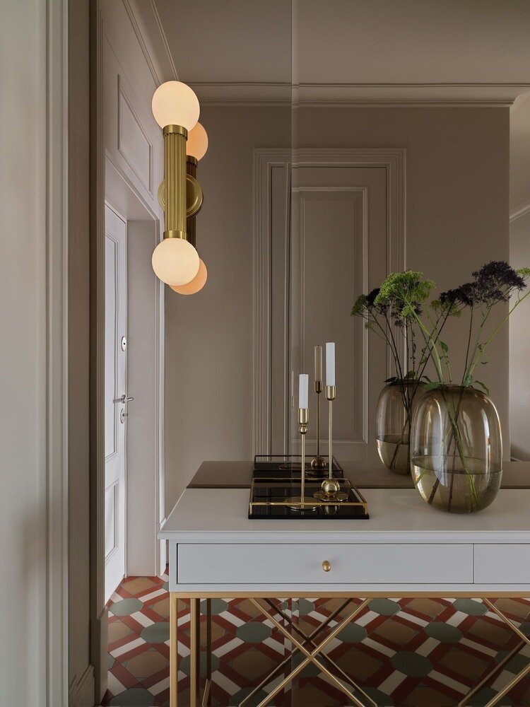 В прихожей слева от входа находится дверь в гардеробную, напротив — зеркальное панно, которое работает на расширение пространства.