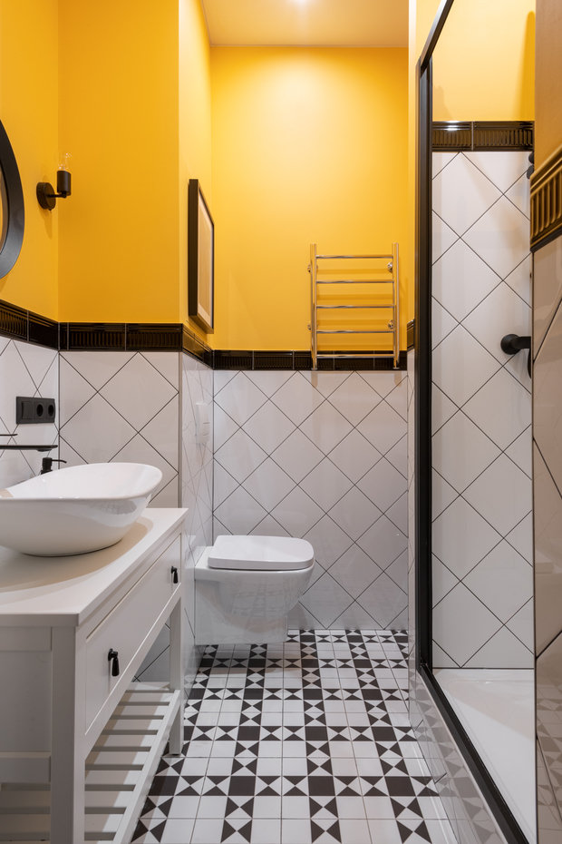 В санузле на полу использована плитка, стены оформили частично плиткой с бордюром, остальные стены покрасили в яркий желтый цвет.