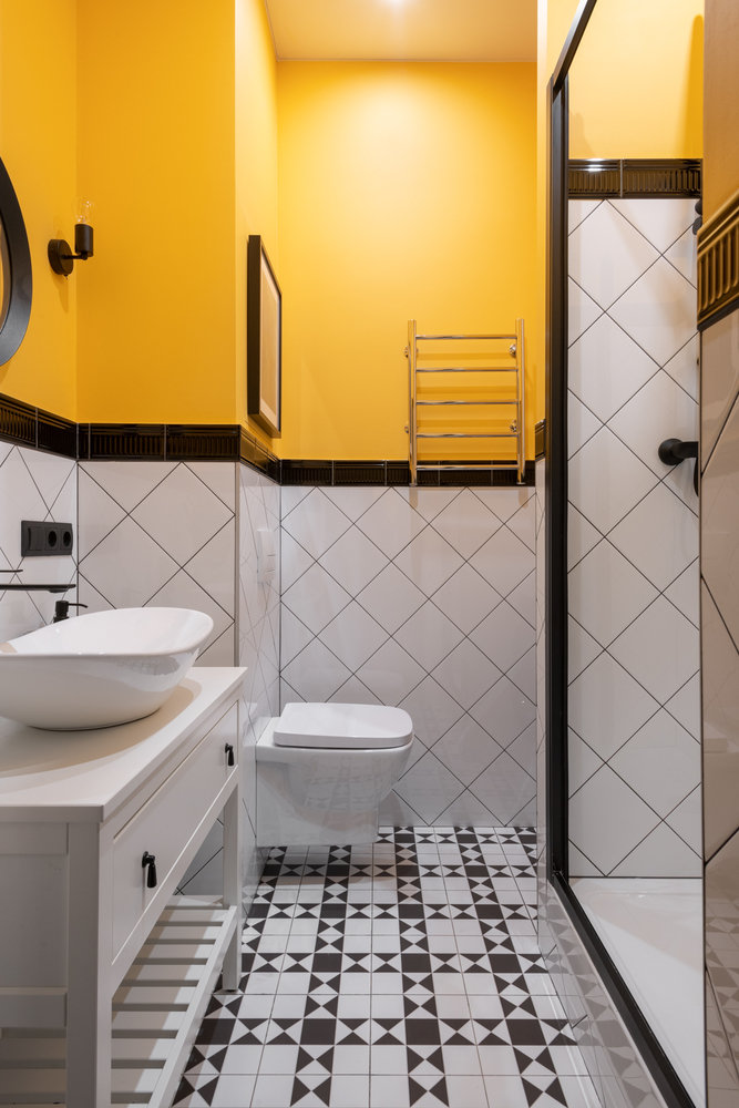 В санузле на полу использована плитка, стены оформили частично плиткой с бордюром, остальные стены покрасили в яркий желтый цвет.