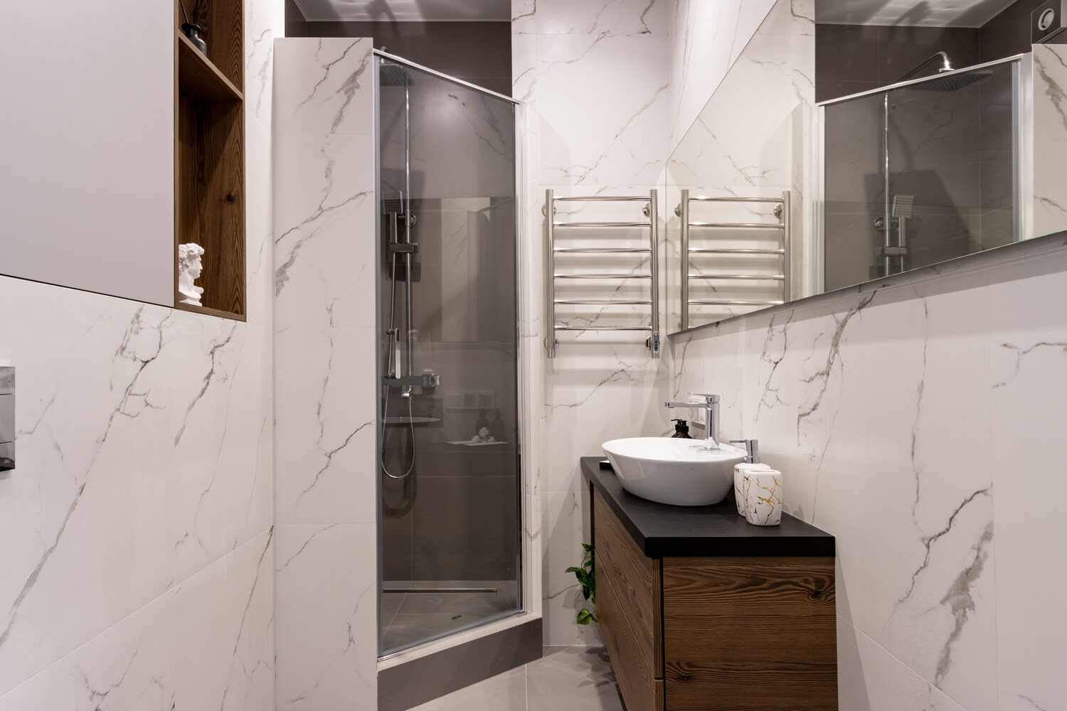 В оформлении санузла использовали керамогранит из двух коллекций. Над раковиной разместили зеркало шириной во всю стену. Получилось стильно, а акцент добавили за счет дерева в мебели и полках. В оформлении санузла использовали керамогранит из двух коллекций. Над раковиной разместили зеркало шириной во всю стену. Получилось стильно, а акцент добавили за счет дерева в мебели и полках.