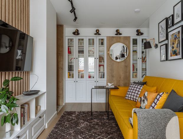 В пространстве между несущими колоннами в гостиной спроектировали встроенные шкафы и закрытые лаконичные полки.