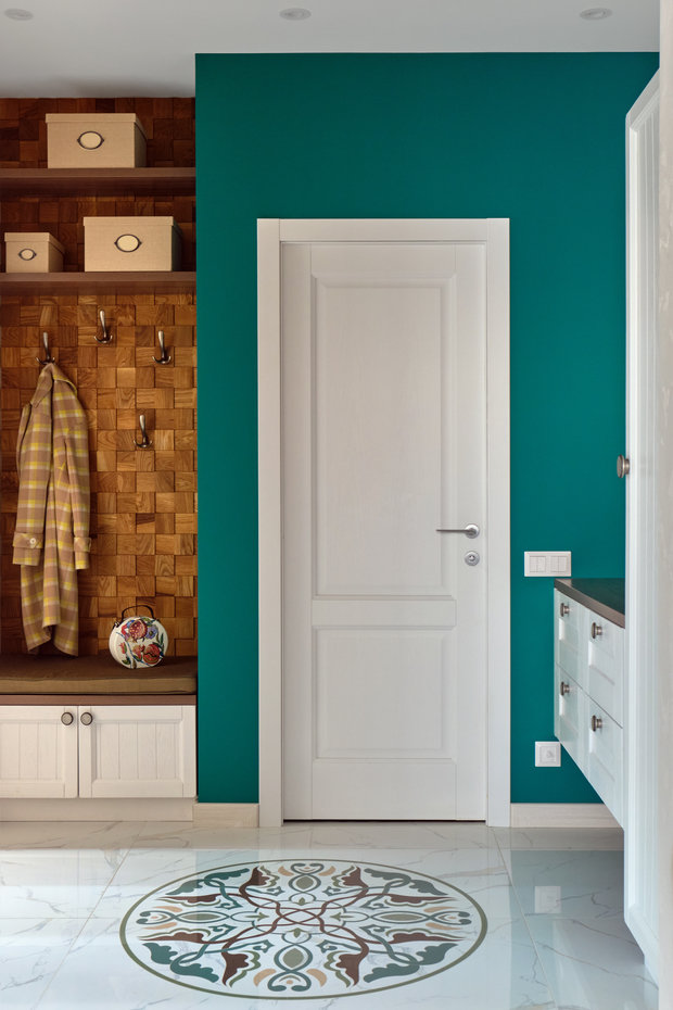 Заказчик хотел вписать в интерьер напольную декоративную розетку. Дизайнер нашла для нее место в прихожей: она стала центром композиции, собирает в себе тона интерьера. Зеленая стена продолжается в кухонном гарнитуре и диване в гостиной.