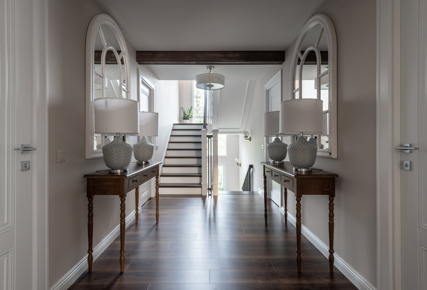 В холле на втором этаже консоли с арочными зеркалами в белых рамах и крупные настольные лампы.