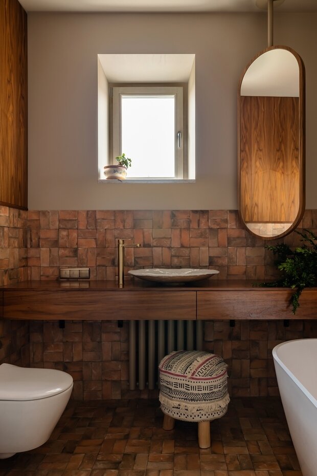 Уровень отделки плитки на стенах был занижен, чтобы помещение приобрело характер комнаты и в нем было максимально комфортно. В отделке использовали плитку терракотовой гаммы, которая напоминает плитку ручного исполнения. Для релаксирующего настроения вечером можно включить подвесной светильник аморфной формы, который бросает живописные блики на стены.