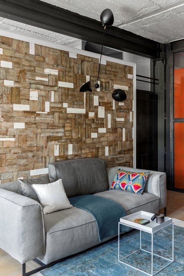 Отделяющая гостиную от кабинета стена, возле которой стоит диван, декорирована паркетом, найденным в этой же квартире при производстве демонтажных работ. По специальной технологии паркет законсервировали вместе с собранной им за десятилетия пылью, а затем покрыли лаком.