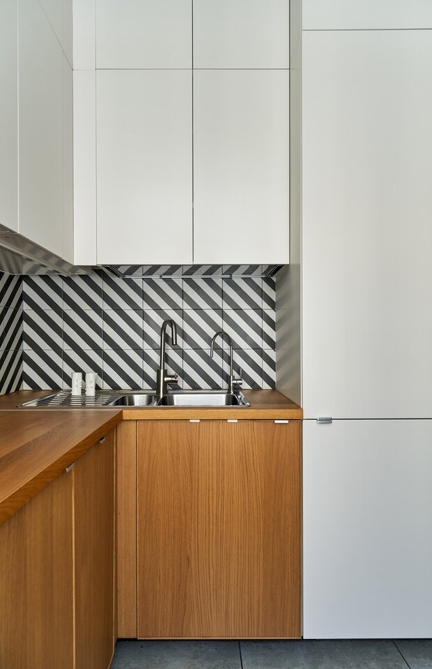 Дизайнеры старались по максимуму использовать пространство, в том числе и по вертикали. На небольшой площади разместили встроенный холодильник, небольшую духовую печь с функцией СВЧ, стандартную варочную поверхность, мойку с крылом и посудомоечную машину. Верхние ярусы кухни предназначены для хранения редко используемых вещей. Весь гарнитур был собран в ИКЕА из стандартных модулей.