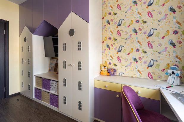 В детской на фасадах шкафов сделаны очень интересные акценты в виде окошек. В целом шкаф выполнен в виде большого дома: боковые домики — отделения для одежды, у каждой дочки своя секция. Центральный домик — для игрушек и телевизора. 