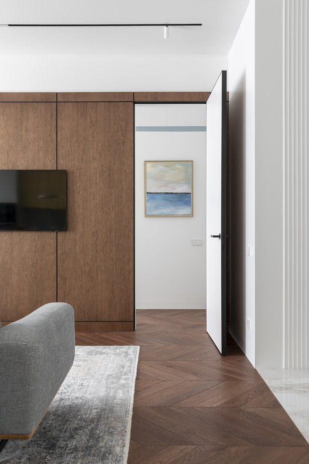 Акцентом в гостиной стала стена из шпона ореха. Дверь в комнату также замаскировали под панель, чтобы она не бросалась в глаза.