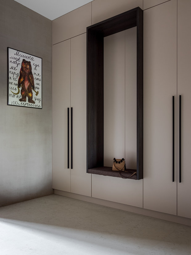 Несмотря на свои внушительные габариты, шкаф в прихожей не выглядит громоздким, потому что в него интегрировали сиденье. Оно изготовлено особым образом по эскизам дизайнеров и не мешает открыванию створок, за которыми находятся крючки для сумок.